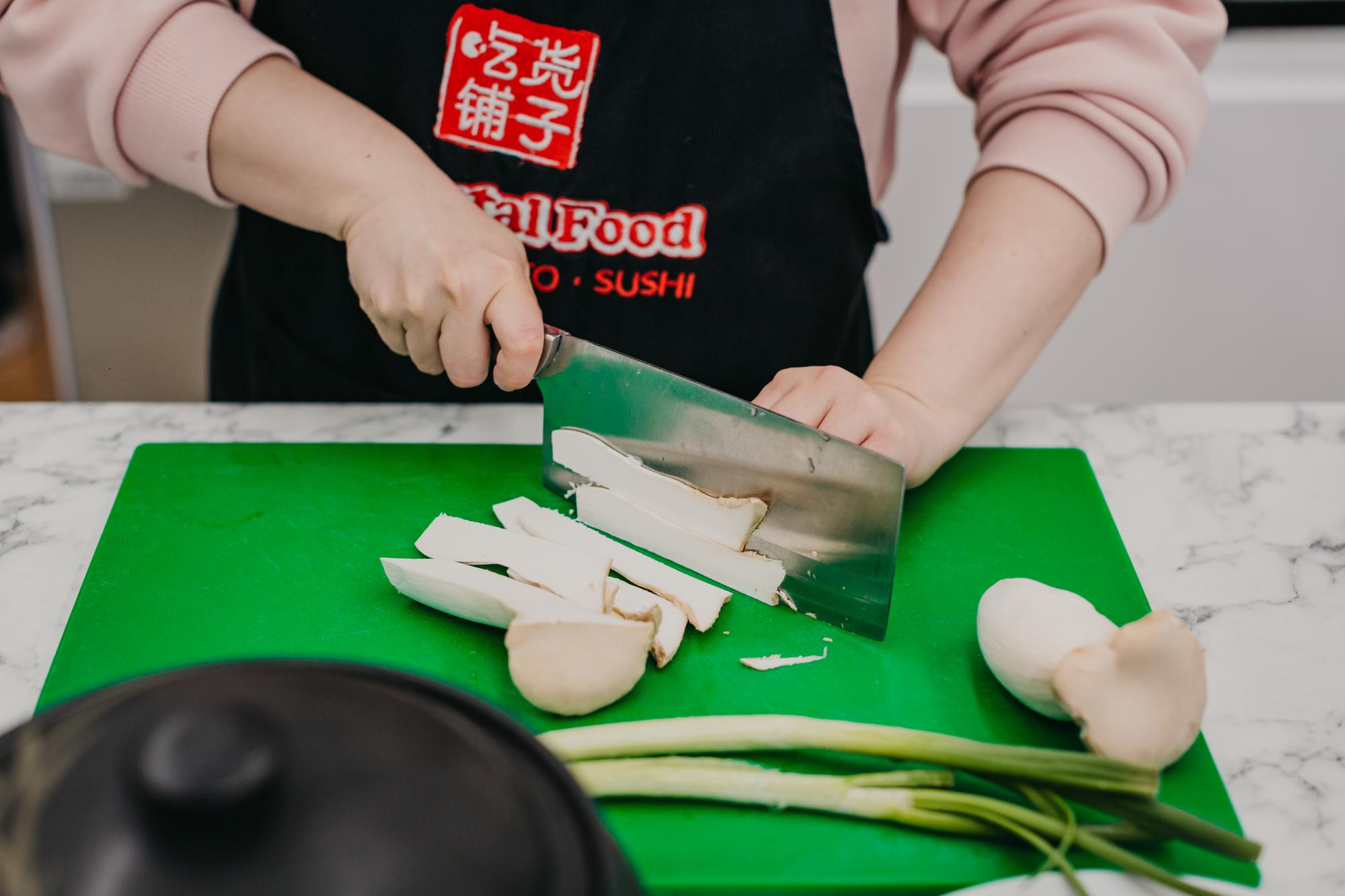 Person slicing a variety of Chinese vegetables on a green cutting board
